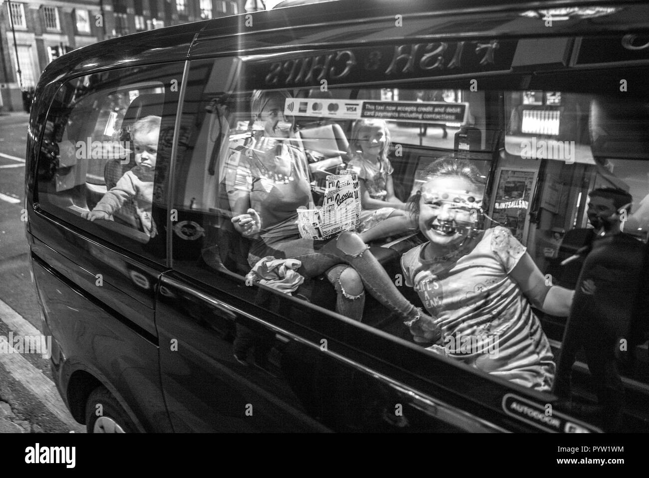 Familia en taxi fuera de la tienda de pescado y chips de Londres .madre y tres niños en el coche sonriendo a la cámara Un niño se ve infeliz Foto de stock