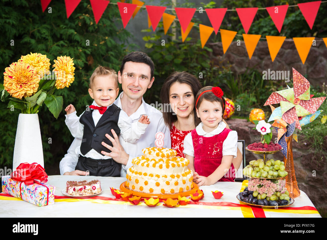Una familia de cuatro personas padre madre hijo e hija celebra el cumpleaños  de su hija de tres años sentado en un festivo decorado decoración de la  mesa y un delicioso pastel