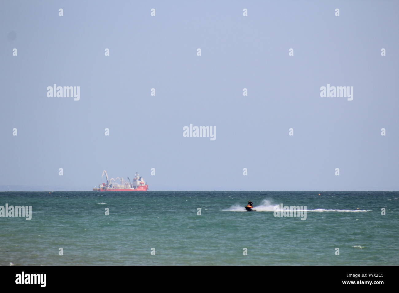 Jet ski en el canal de la mancha con un barco de carga en la distancia Foto de stock