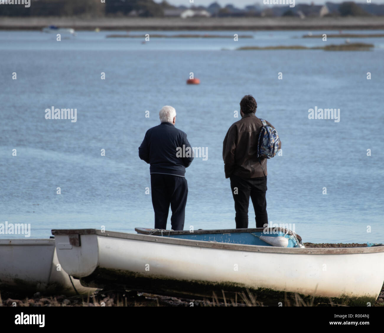 Anciano padre y crecido hijo mirando a ver en la costa con un viejo barco de madera en primer plano Foto de stock