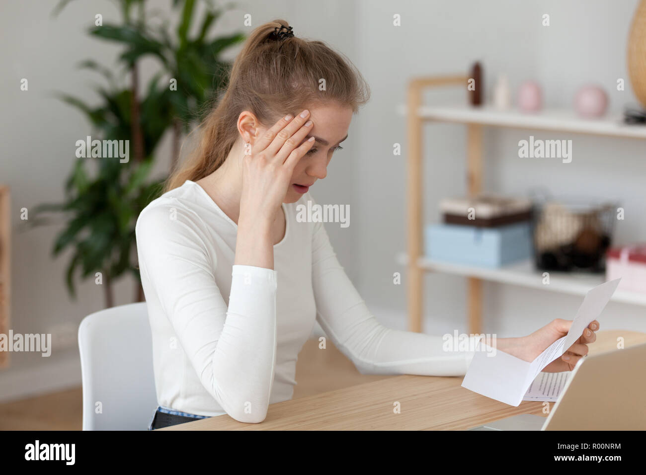 Frustrado chica desagradable leer carta sentado al escritorio Foto de stock