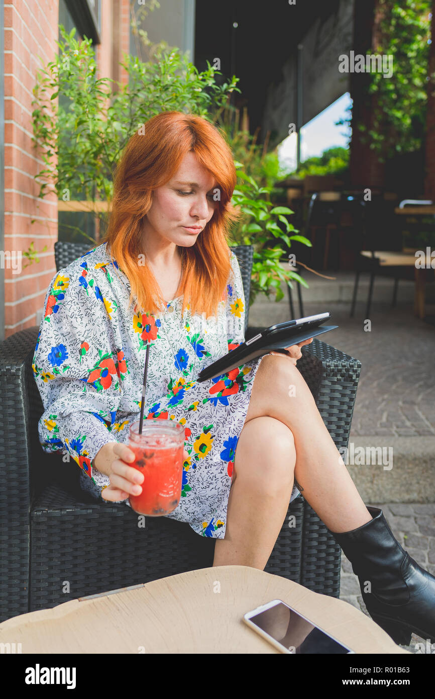 Hermosa mujer sentada al aire libre para adultos con bebida con tablet - tecnología, pequeña empresa, concepto de trabajo remoto Foto de stock
