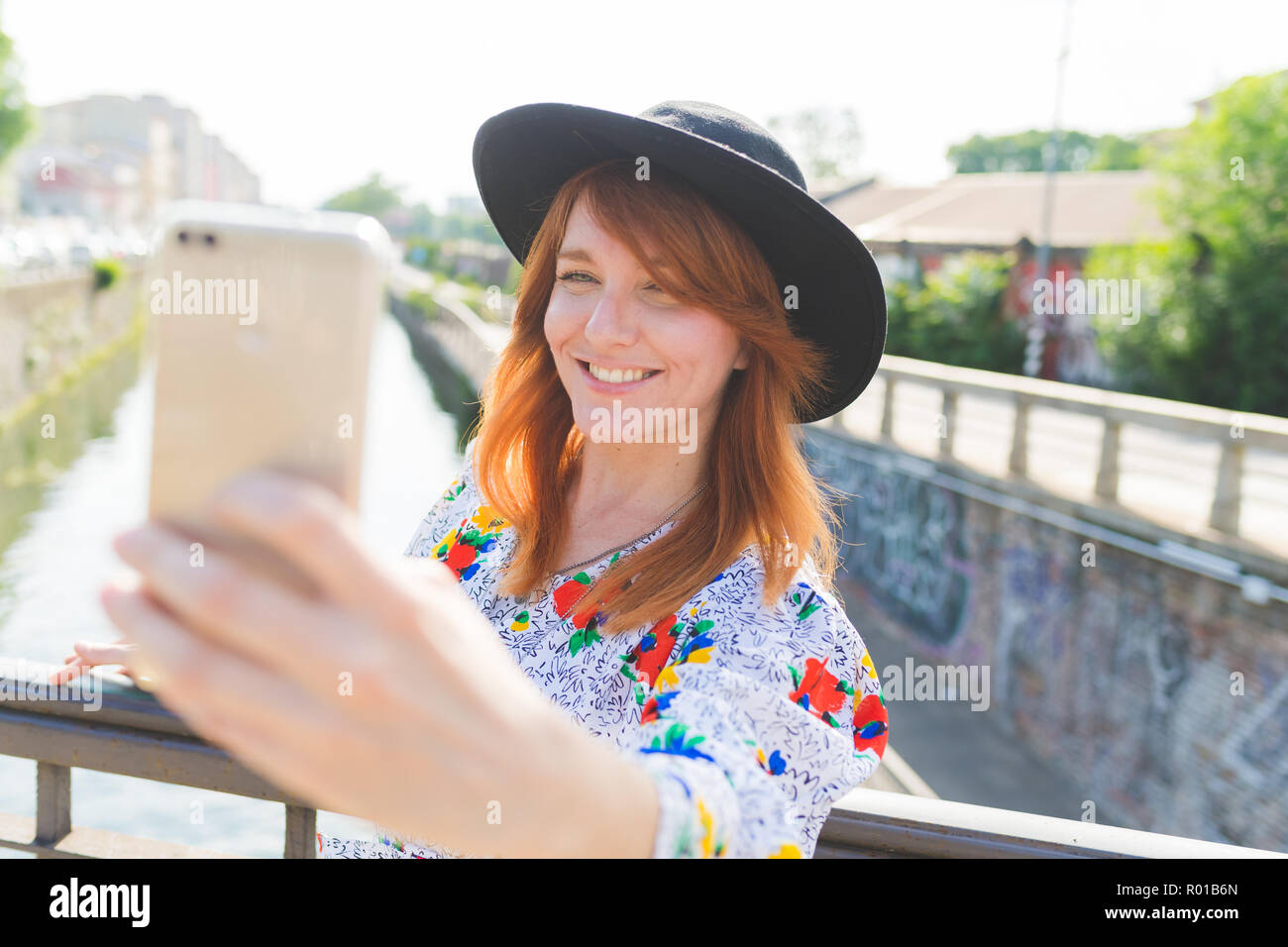 Bella mujer adulta luz trasera exterior utilizando smart phone teniendo selfie sonriendo - red social, compartir, concepto tecnológico Foto de stock