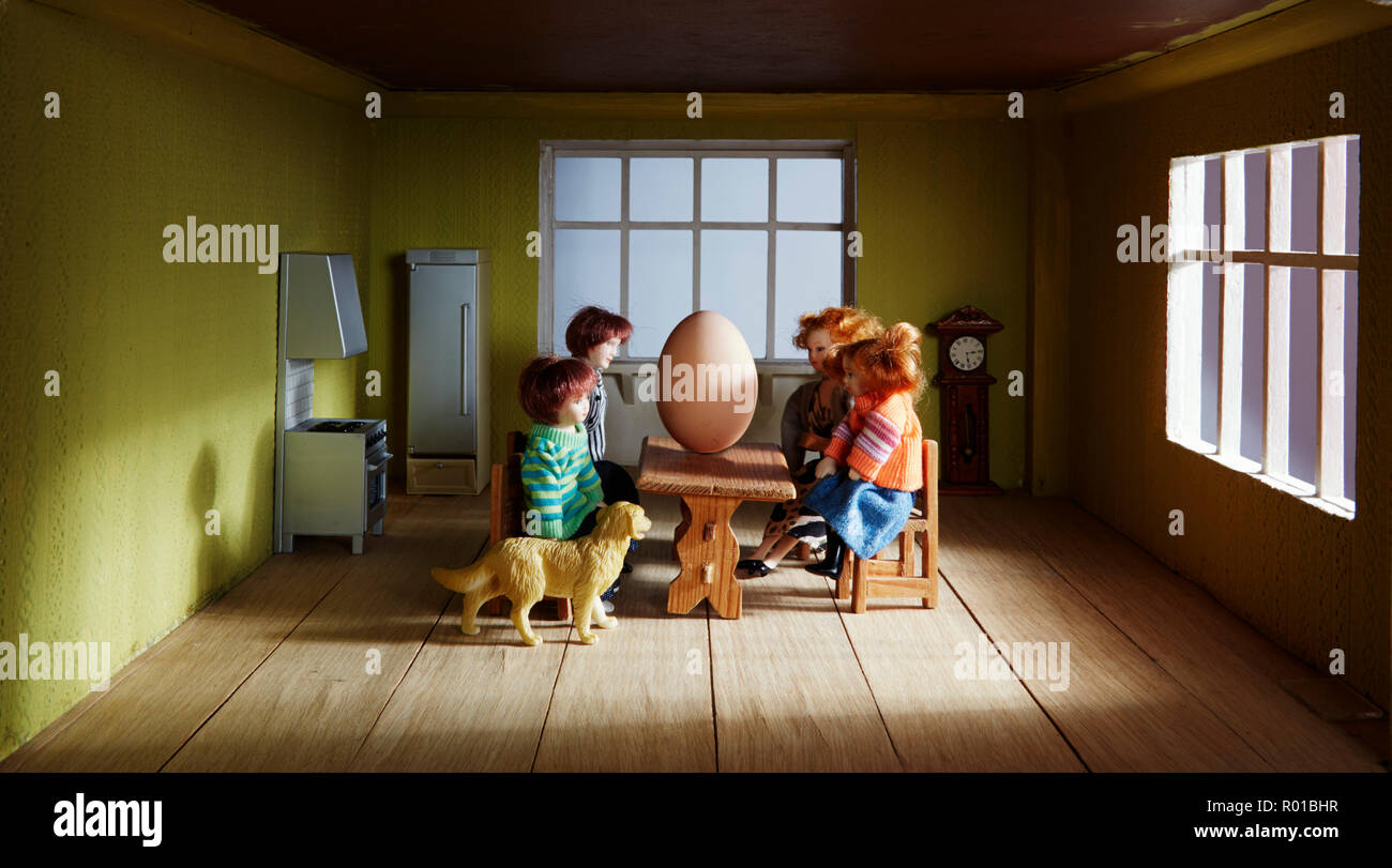 En el interior de una casa de muñecas con una familia sentada en una mesa con un huevo gigante en la mesa Foto de stock