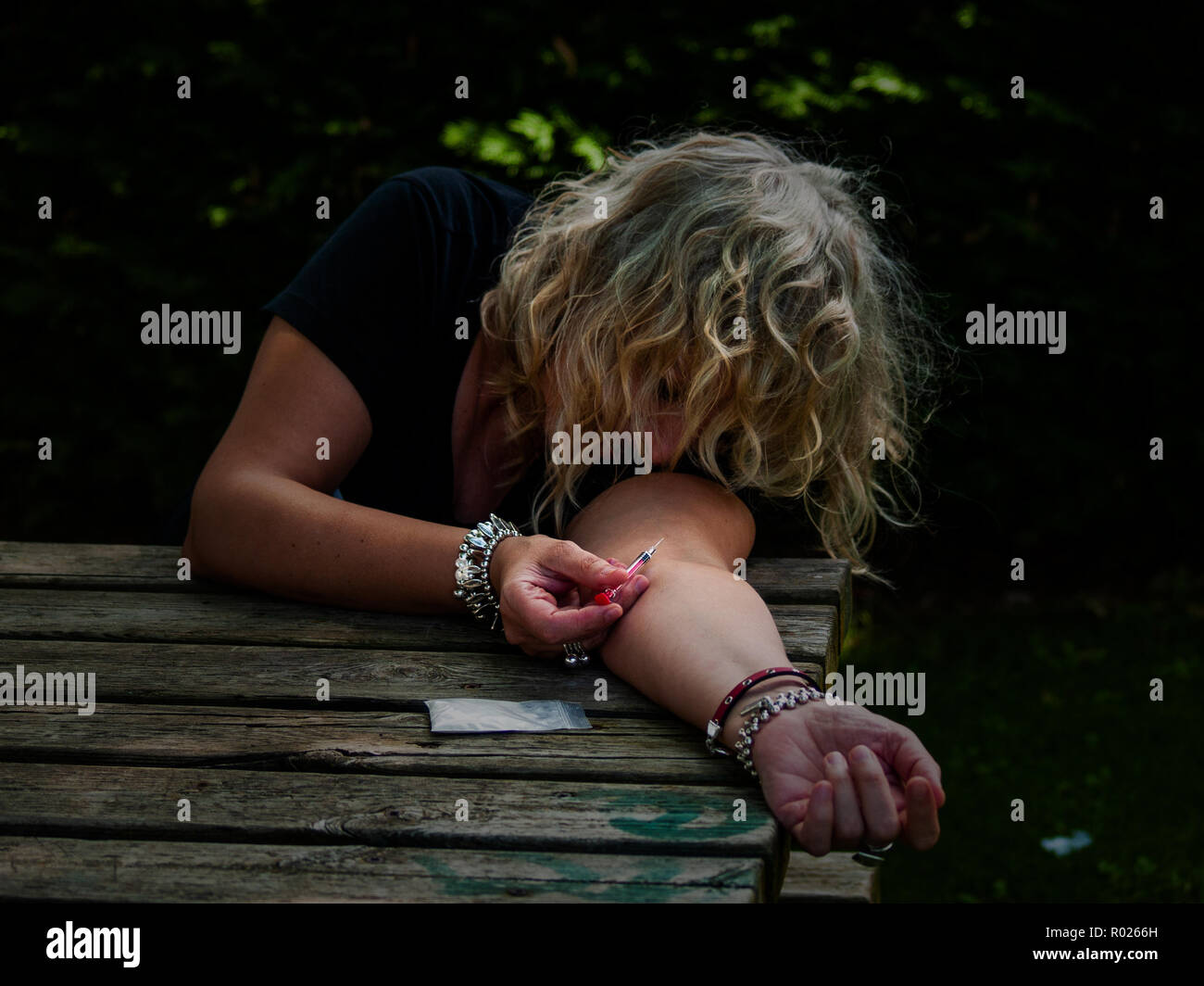 Una mujer de drogas inyectables en su brazo con una jeringuilla en la calle y una dosis de medicamento para el lado Foto de stock