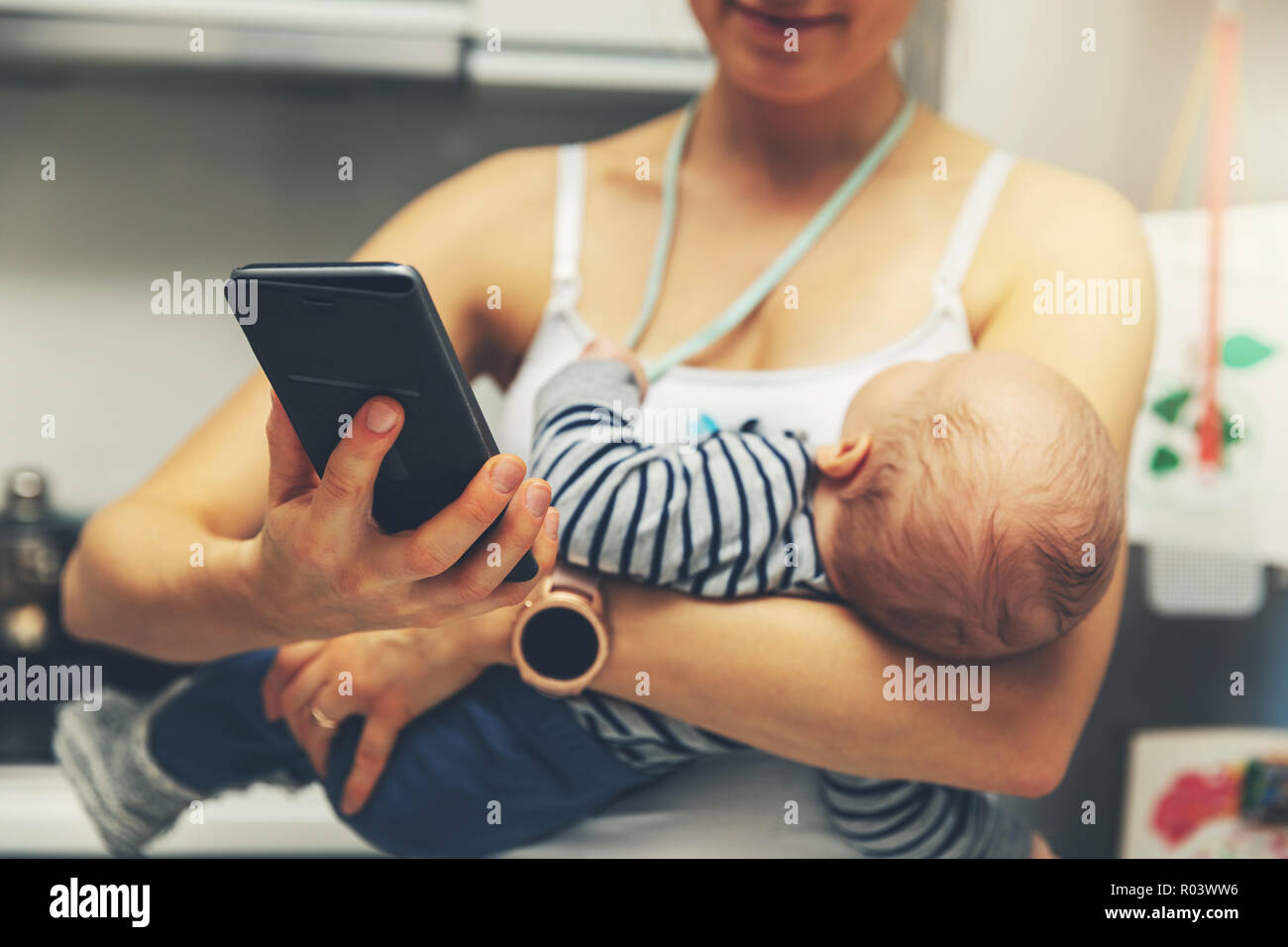 La madre está utilizando el smartphone mientras mantiene el bebé lactante Foto de stock