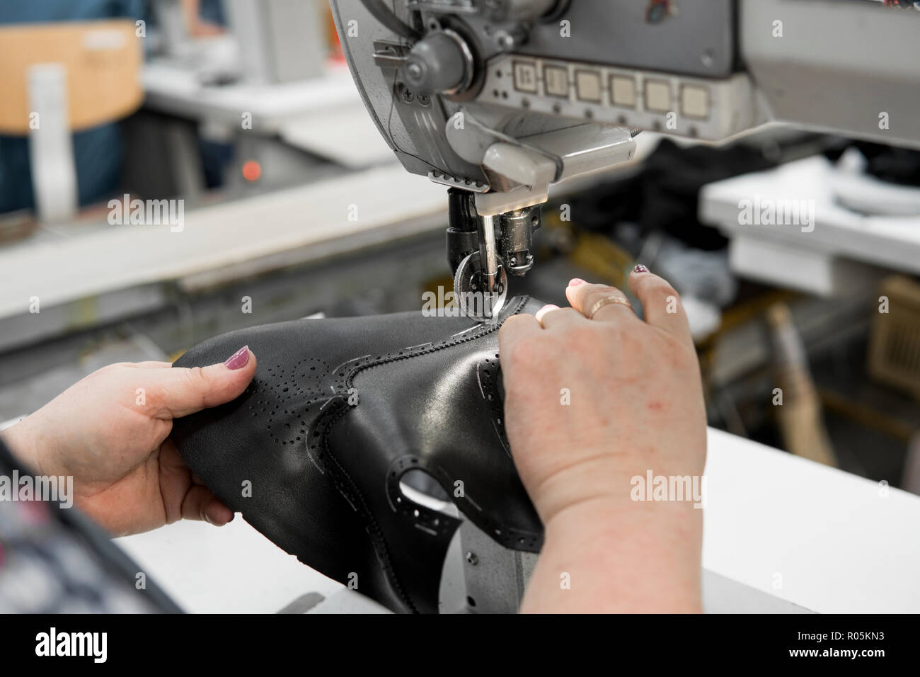 Máquina de coser en un taller de cuero en acción con manos trabajando en  detalles de cuero para calzado. Manos de mujer vieja con la máquina de coser  en la fábrica de