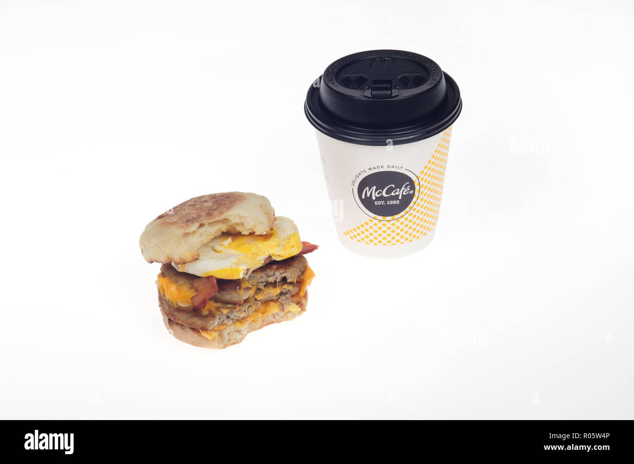 McDonald's Triple Stack egg mcmuffin sándwich w/2 salchichas empanadas 2 tiras de tocino 2 lonchas de queso americano en panecillo inglés con mordida tomado & Coffee Foto de stock