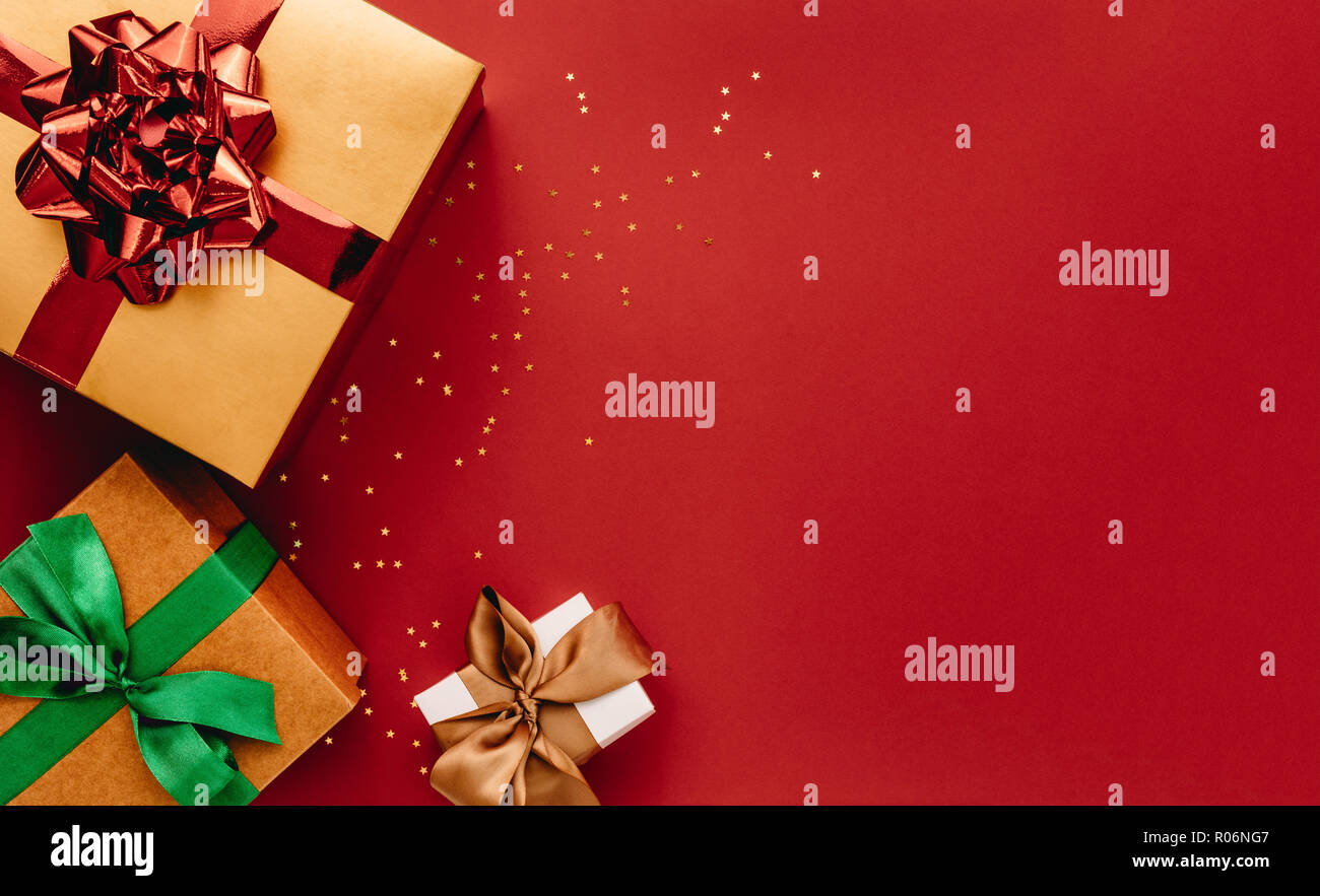 Montón de cajas de regalo y estrellas confetti sobre fondo rojo. Composición laicos plana para la Navidad con espacio de copia. Foto de stock