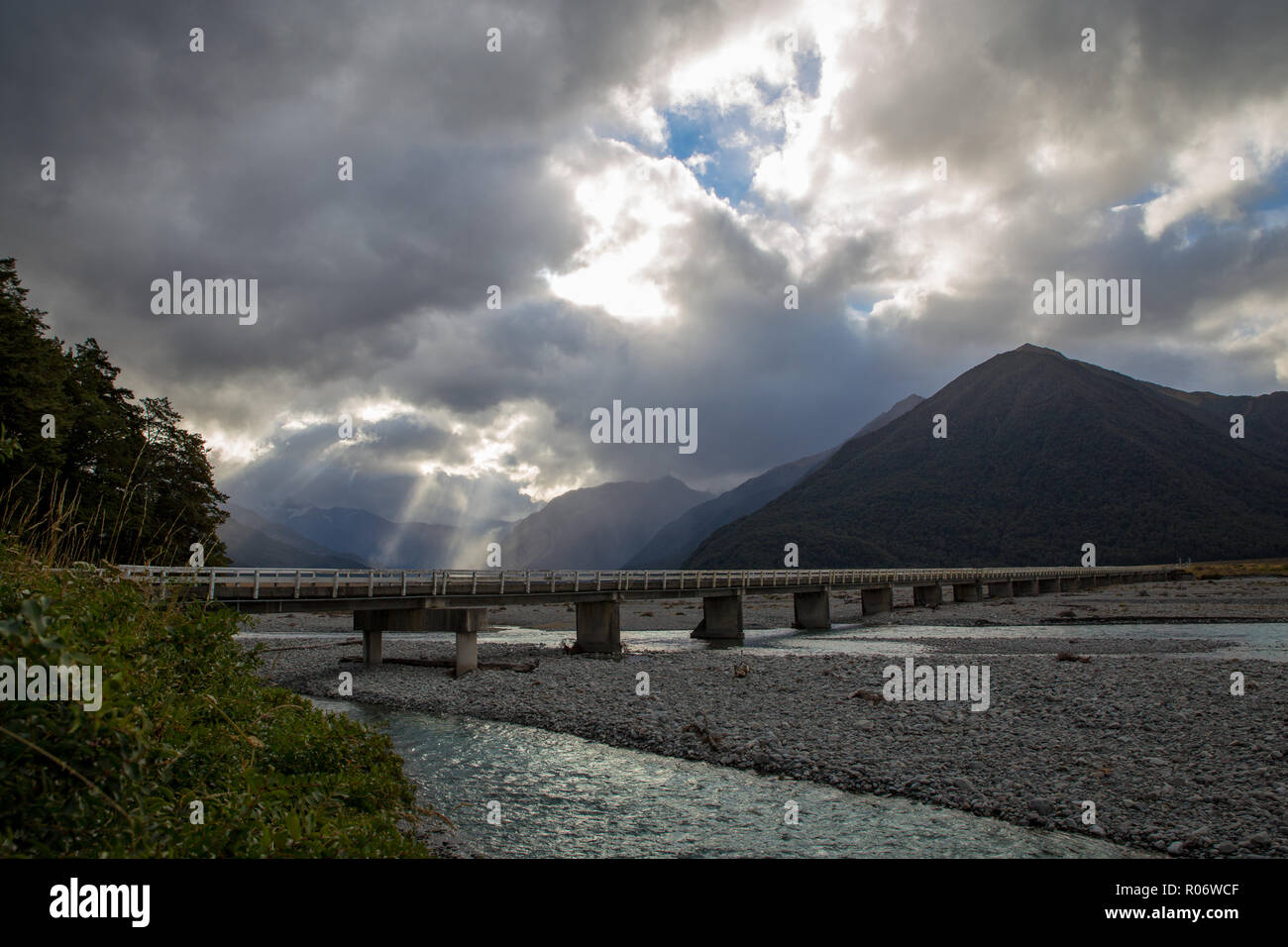 Un largo puente cruza un río trenzadas en un valle alpino, Canterbury, Nueva Zelanda Foto de stock