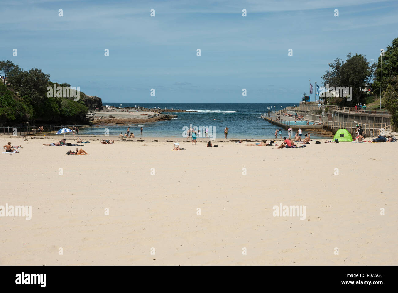 Vista de la playa de arenas doradas de la playa Clovelly, Sydney, con gente tomando el sol y nadando en el mar y a la derecha hay una piscina. Foto de stock