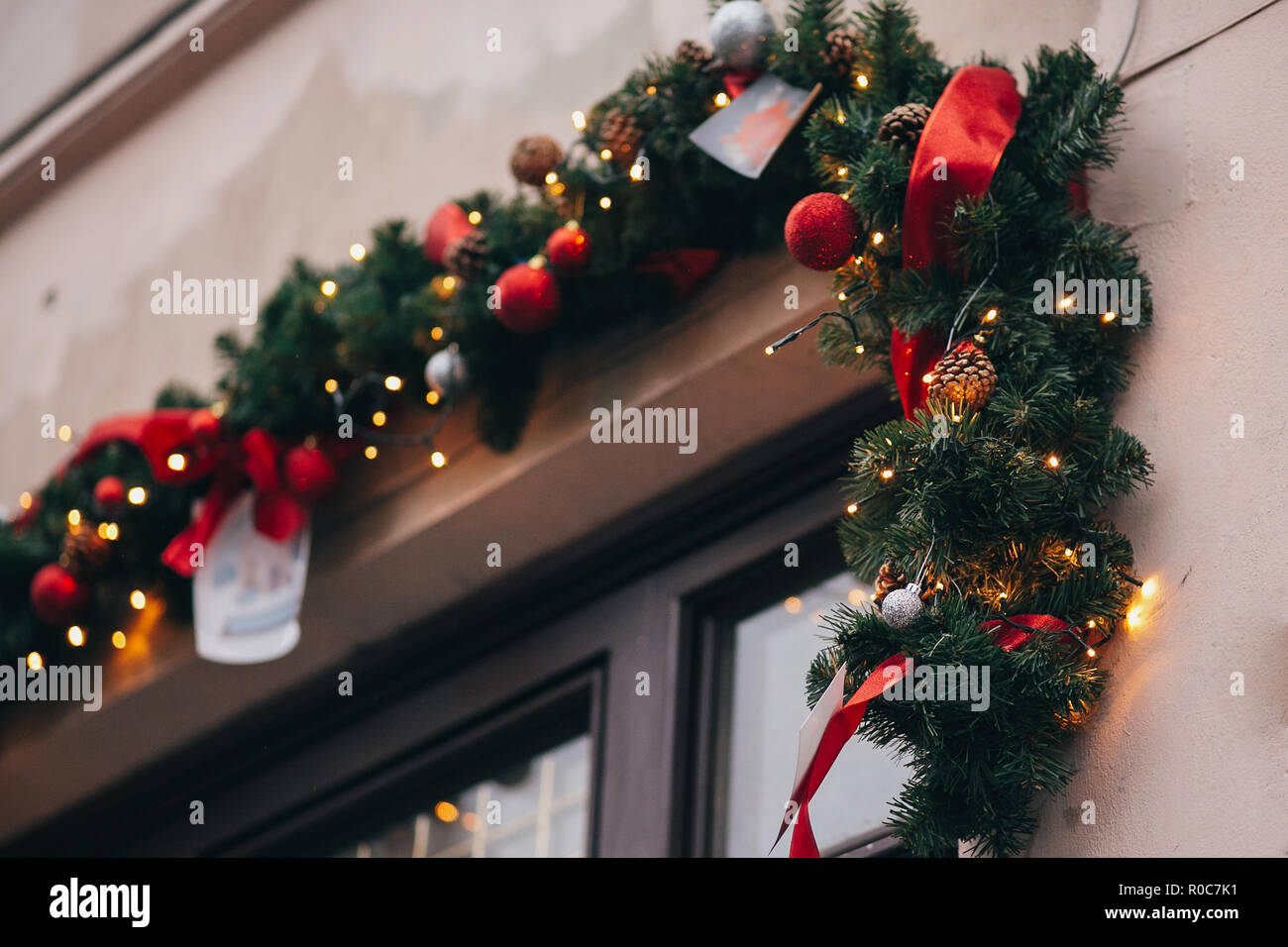 Sin permanecer exprimir Elegante decoración de navidad, guirnaldas y luces de ramas de abeto con  adornos de color rojo en la ventana en la unión de las calles de la ciudad.  Iluminación y decoración festiva