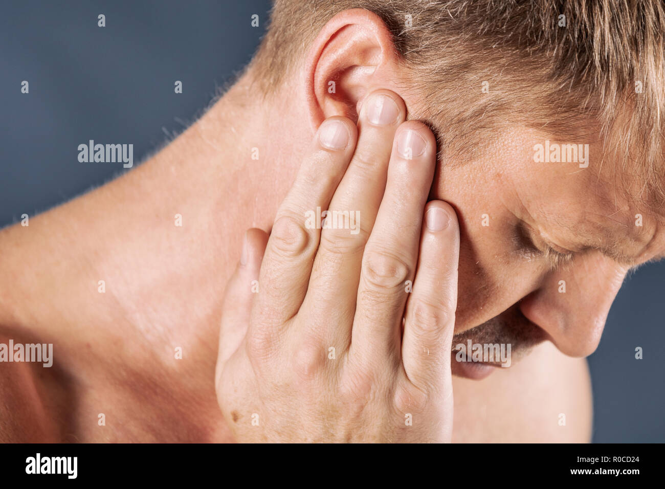 El hombre tiene un dolor de oído. El hombre sufre de otitis sobre fondo azul. Foto de stock
