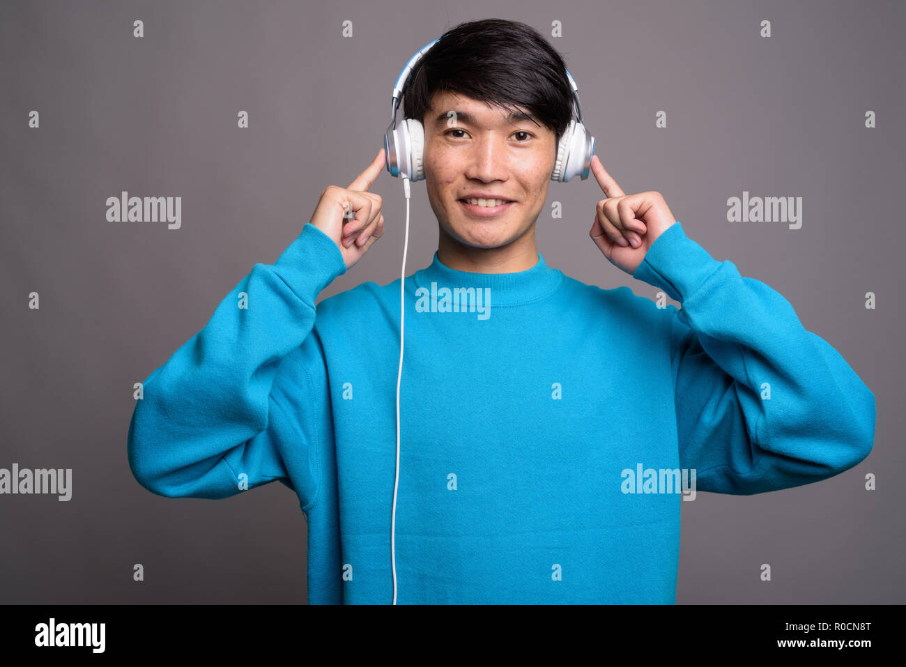 Joven hombre asiático escuchando música contra el fondo gris Foto de stock