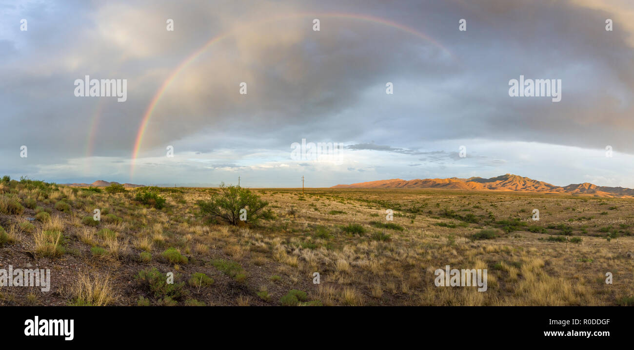 Un doble arco iris visible para el medio como sol en el desierto alto de SE, Arizona (panorama) Foto de stock