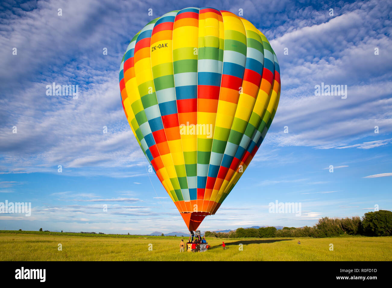 Un colorido globo de aire caliente llevando turistas aterriza en un campo en el campo en Nueva Zelanda Foto de stock