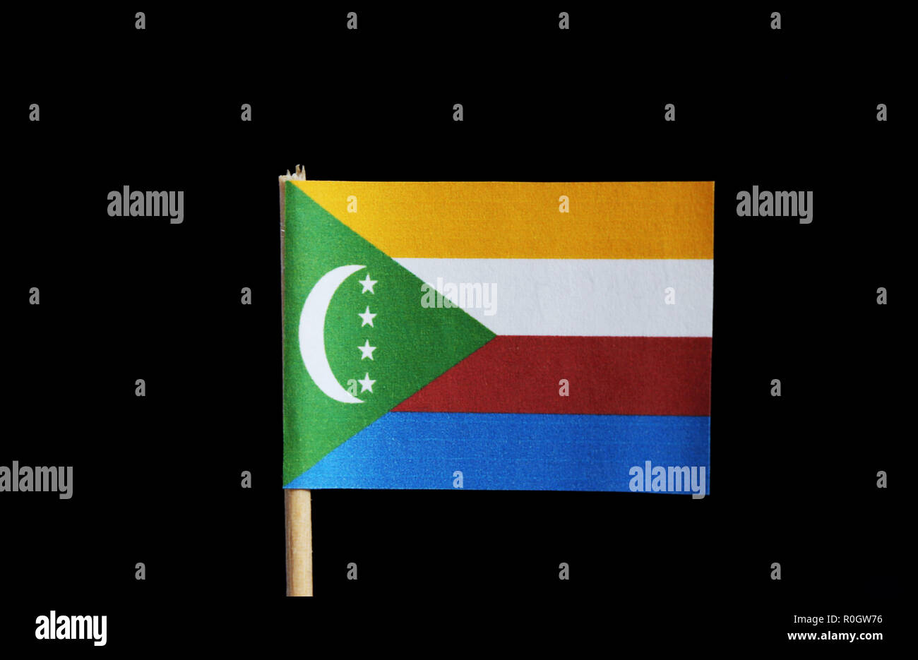 Una bandera nacional de las Comoras en un palillo sobre fondo negro. Cuatro  franjas horizontales de color amarillo, blanco, rojo y azul con un verde  chevron basado en Fotografía de stock -