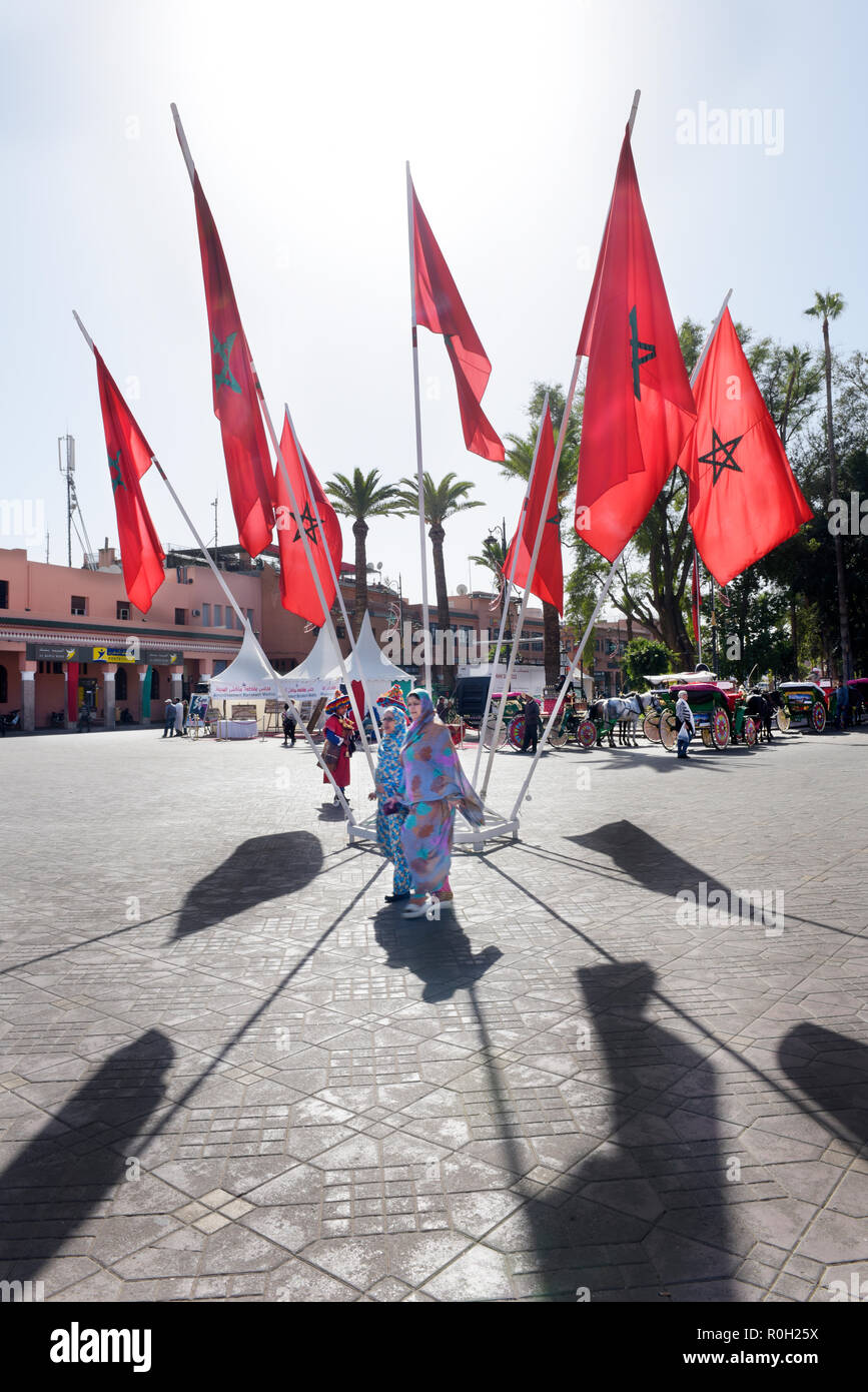 Dos mujeres del Norte de África se precipitan en las calles de Marrakech en la plaza Jamaa el Fna, rodeado por el círculo de las banderas marroquíes Foto de stock