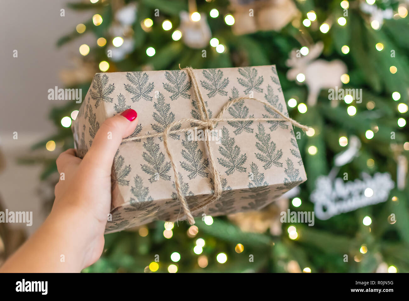 Mano sosteniendo un regalo para el árbol de Navidad. el nuevo año 2019.  loft árbol en estilo rústico, don atados con una cuerda Fotografía de stock  - Alamy