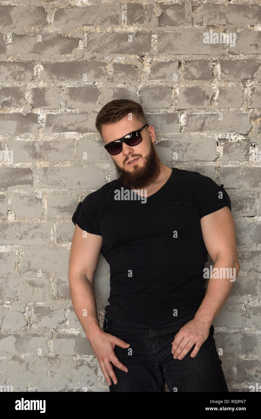 El carrocero en gafas de sol vertical. Hombre musculoso con barba en la ceñida  camiseta permanente en la pared de ladrillo. Elegante y deportivo joven  Fotografía de stock - Alamy