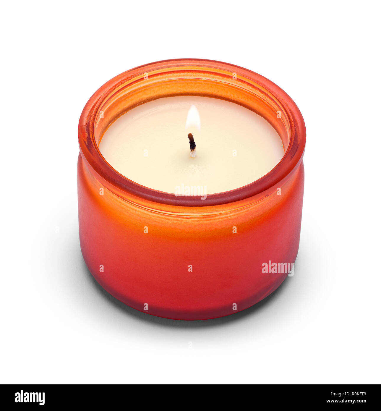 La pequeña vela encendida en cristal naranja aislado sobre un fondo blanco. Foto de stock