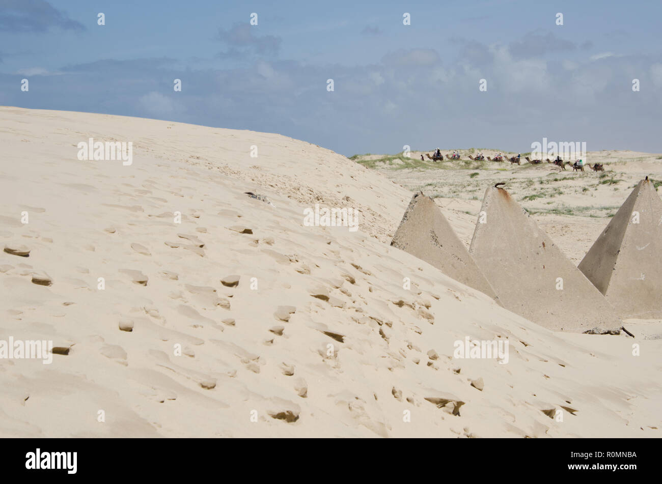 Soñando con el desierto del Sahara aventura. Los jinetes de camellos en el horizonte a distancia con grandes dunas de arena y piedra con forma de pirámide en primer plano. Foto de stock
