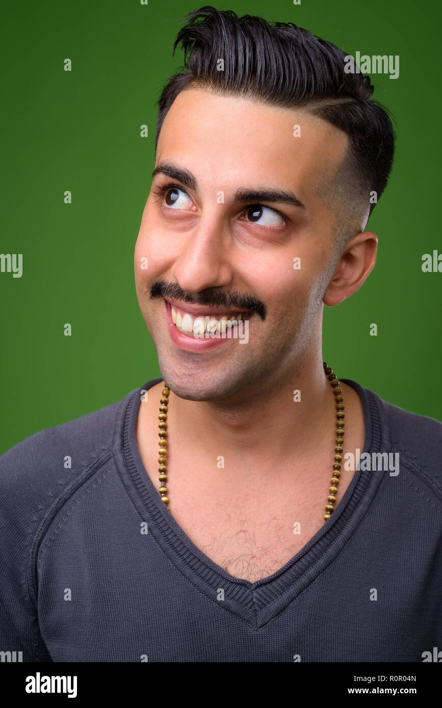 Joven apuesto hombre con bigote iraní contra backgroun verde Foto de stock