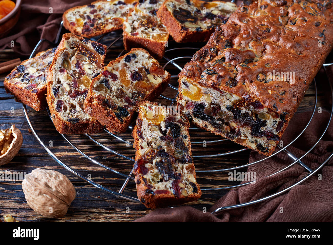 Chunky deliciosos frutos secos rica torta pastel sobre un hilo de soporte con paño marrón, canela, albaricoques secos y frutas en una fecha rústicas de madera tabl Foto de stock
