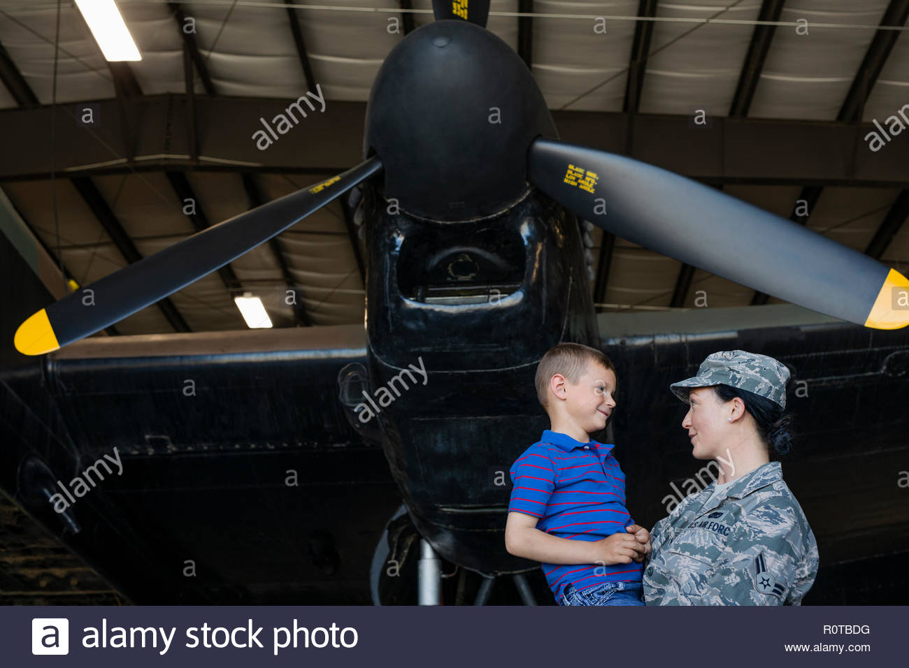 Piloto del ejército femenino madre sosteniendo hijo debajo de avión en avión hangar Foto de stock