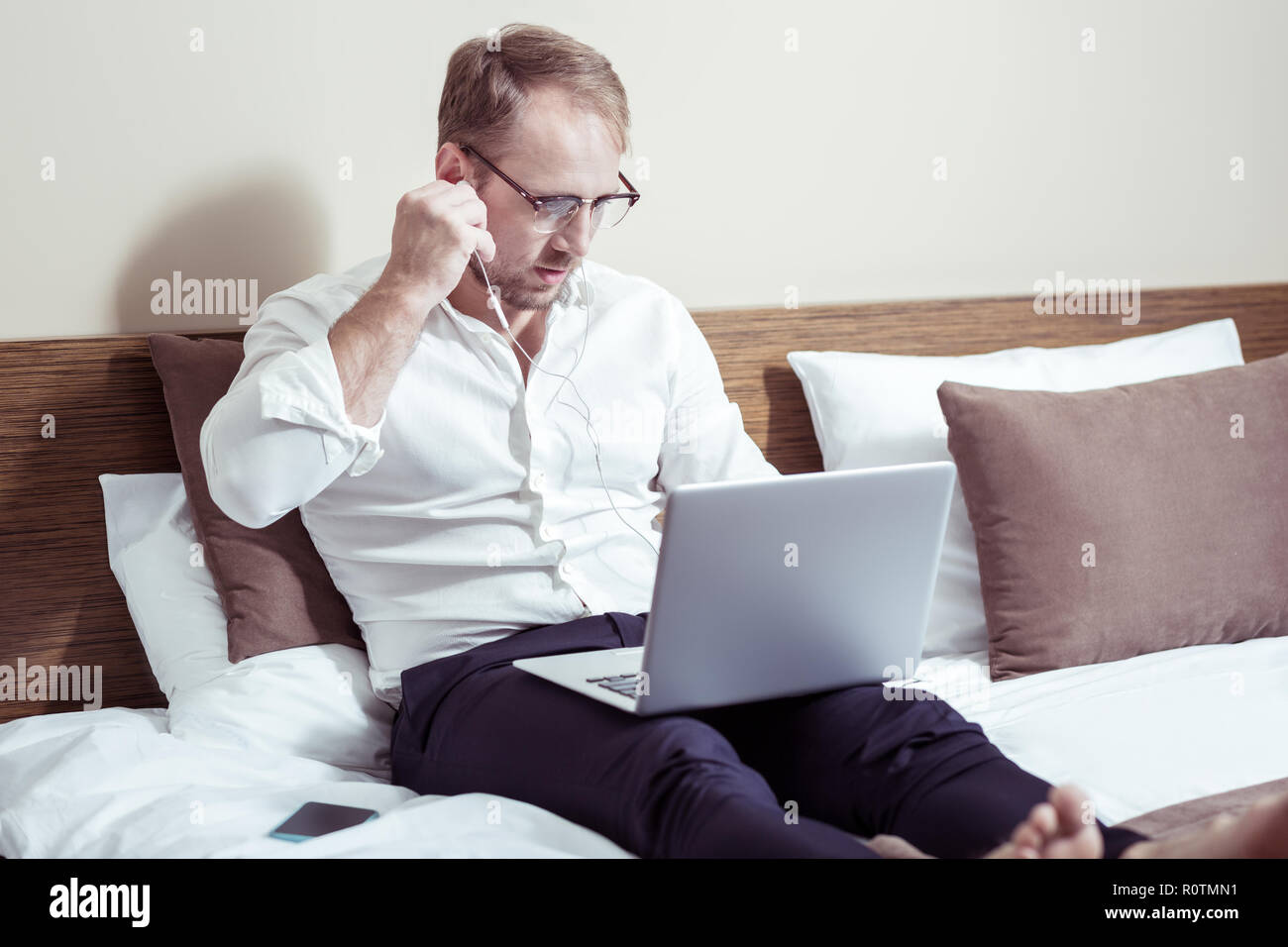 Empresario vistiendo pantalones oscuros y camisa blanca tumbado en la cama de hotel Foto de stock
