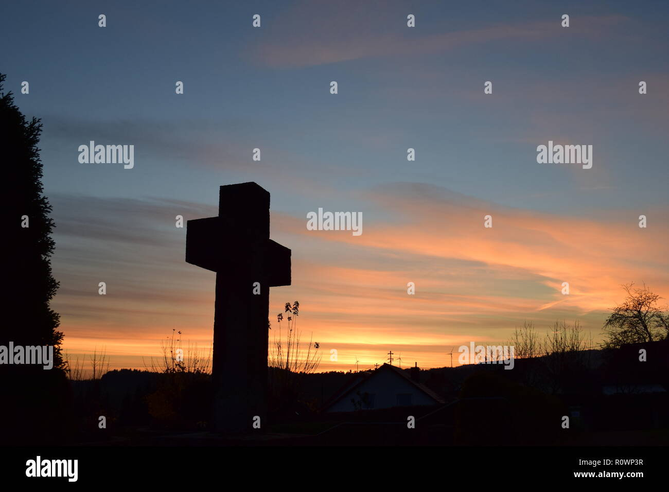 Línea de tiempo de la tarde el Atardecer visto desde el cielo detrás de una cruz de piedra de la escultura de arena durante la puesta de sol sol en el cementerio civil Reimsbach, Sarre, Foto de stock