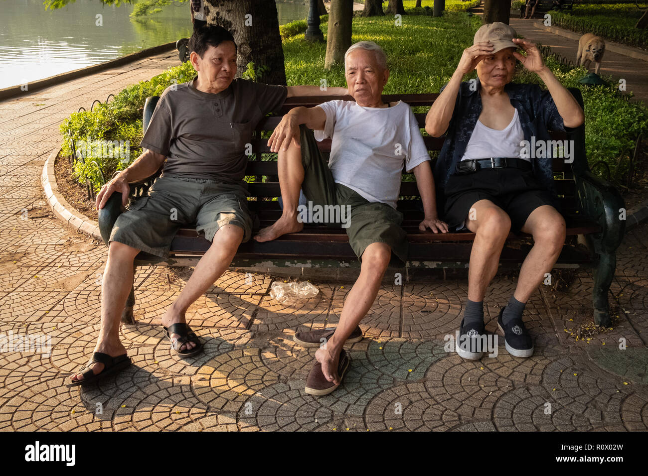 Los hombres de mediana edad hablando sobre un banco del parque por el Lago Hoan Kim, Hanoi, Vietnam. Foto de stock