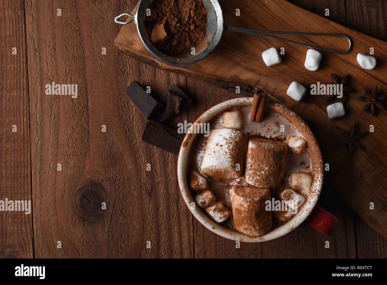 Fotografía cenital de una gran taza de chocolate caliente con malvaviscos sobre una mesa de cocina de madera rústica, con espacio de copia. Foto de stock