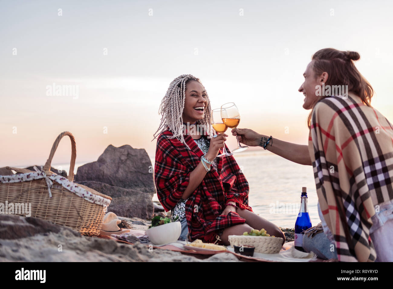 Pareja joven con telas escocesas sobre los hombros con una cena romántica en la playa Foto de stock