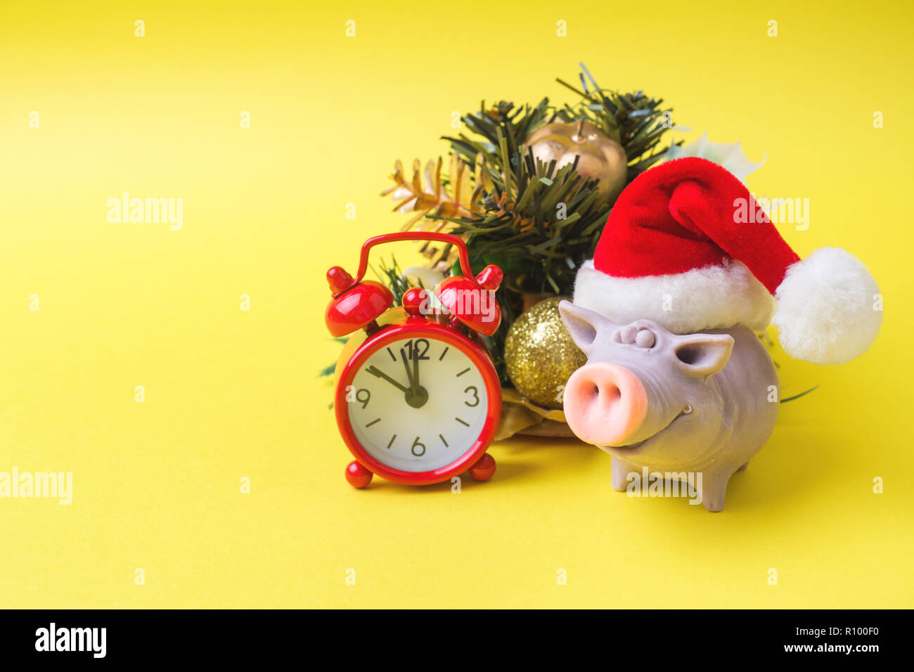 Navidad año nuevo concepto. La figura del cerdo en los conos del árbol gorro  de Papá Noel regalos watch sobre un fondo amarillo. Copie el espacio  Fotografía de stock - Alamy