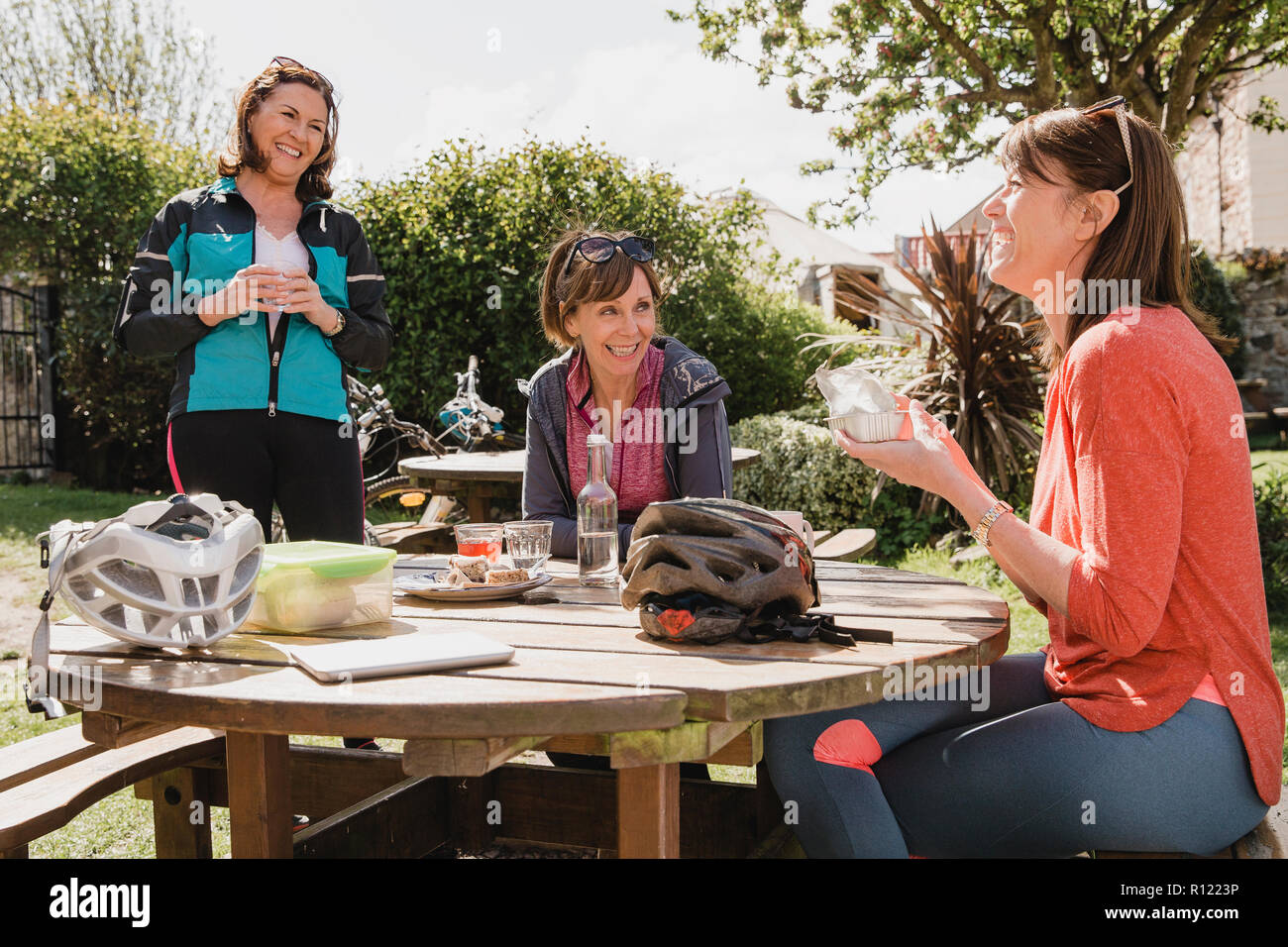 Un pequeño grupo de ciclistas de hembras maduras sentarse en la zona de estar exterior de una cafetería. Tey están disfrutando de un refresco como se tome un descanso. Foto de stock