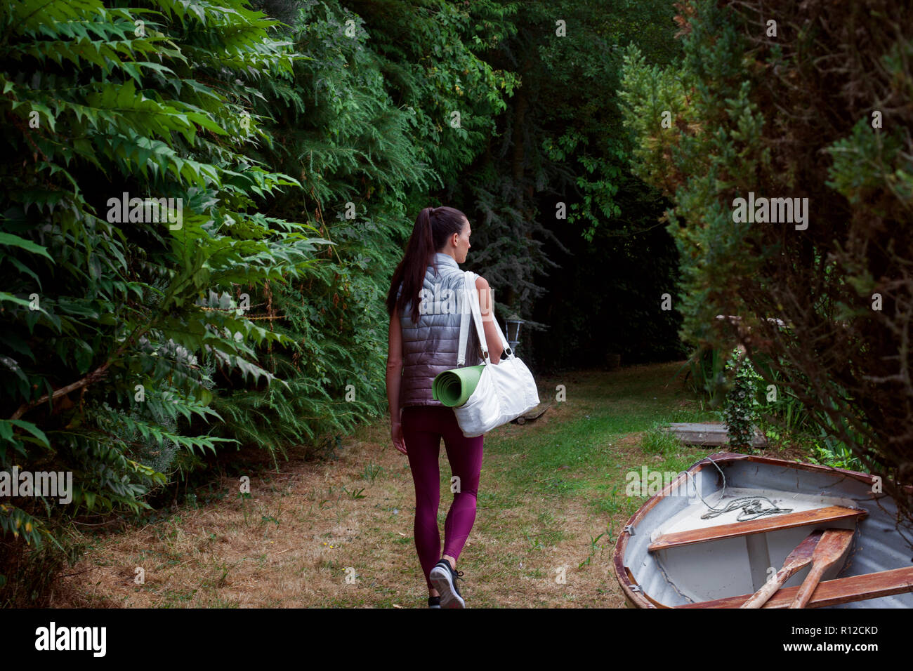 Mujer que llevaba paseando por el jardín de la estera del yoga Foto de stock