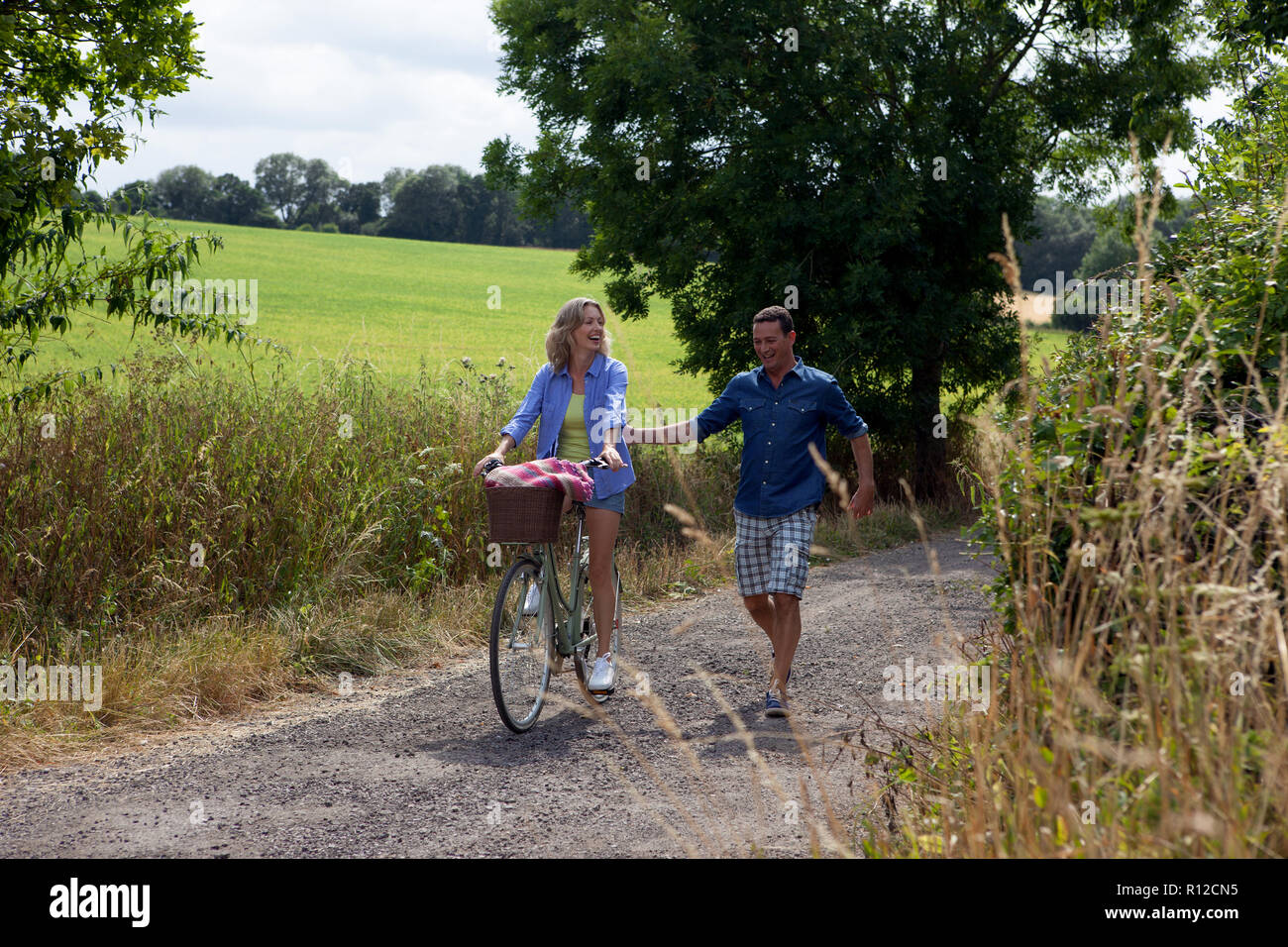 Pareja paseando y ciclismo en carretera rural Foto de stock