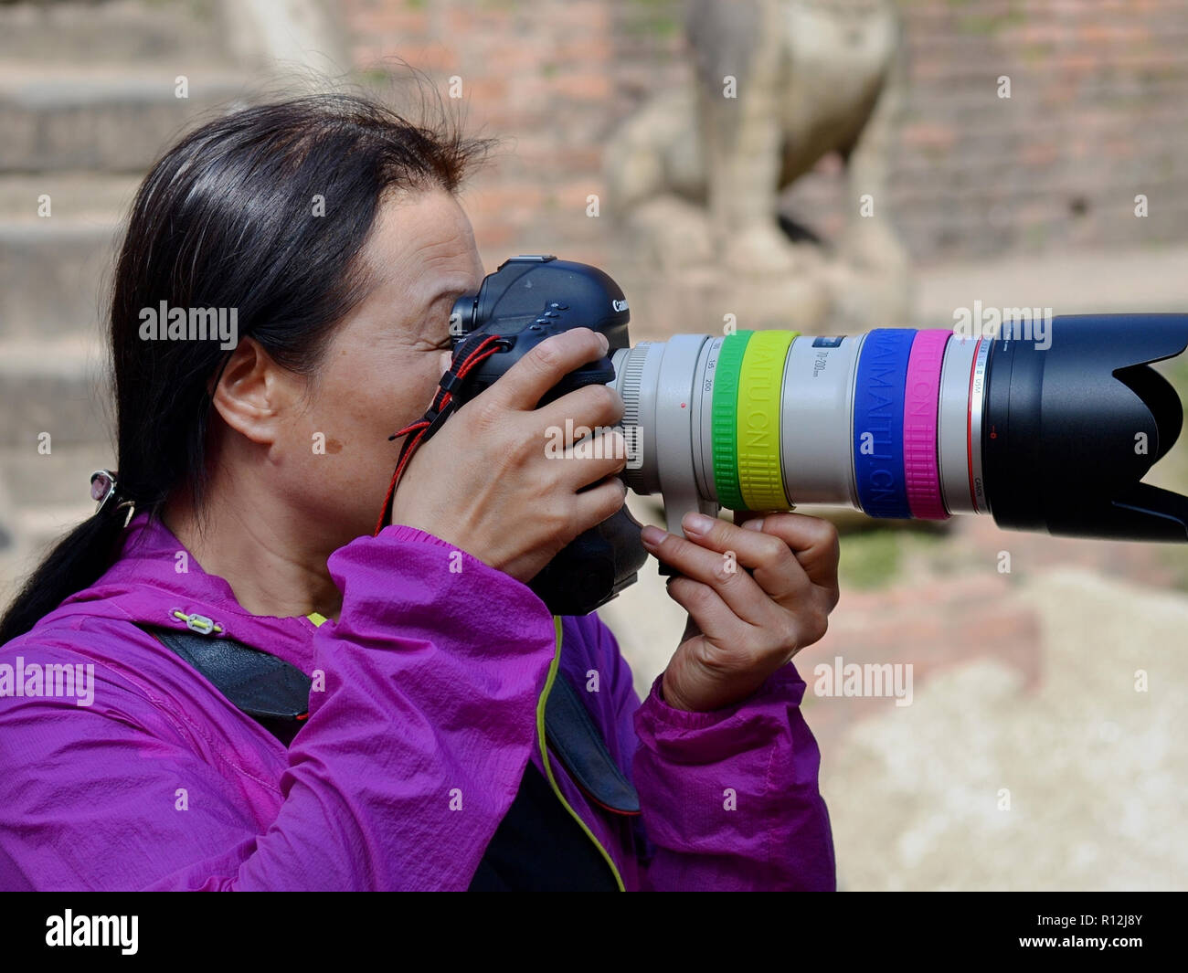 Fotógrafo de calle femenino chino toma una foto con su cámara DSLR de Canon y un teleobjetivo de alta potencia. Foto de stock
