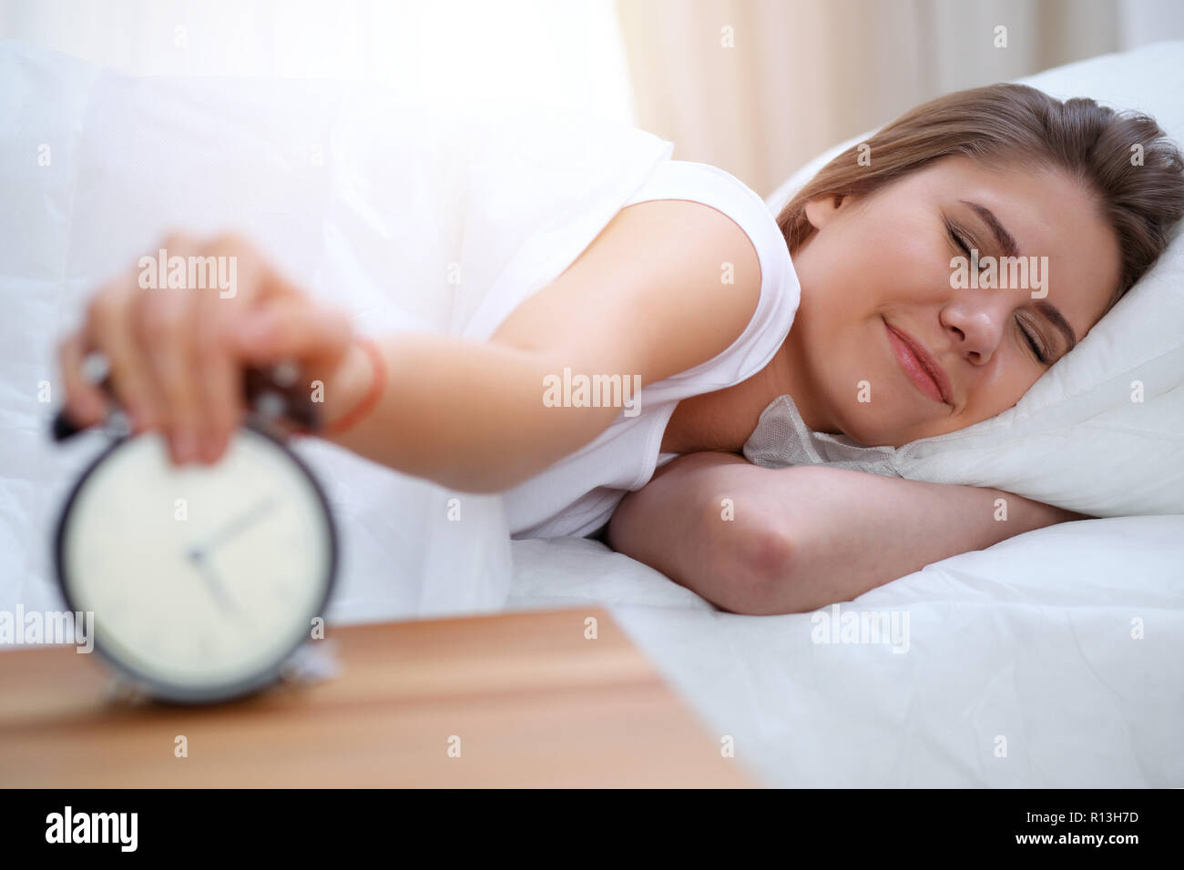 Sleepy joven morenita mujer estirar la mano para sonar la alarma dispuestos apagarlo. Despertar temprano, no dormir lo suficiente concepto Foto de stock