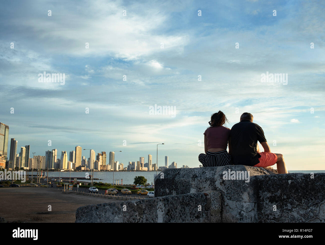 La pareja se asienta en la cima de la pared de piedra de la 'Ciudad Vieja' viendo el horizonte del nuevo barrio Bocagrande. Cartagena de Indias, Colombia. Oct 2018 Foto de stock