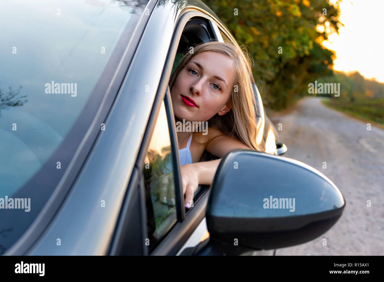 Una joven y bella mujer con cabello largo se sienta al volante del coche y mira por la ventana. Foto de stock