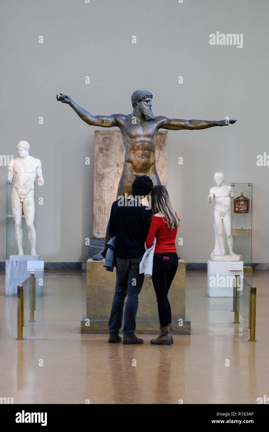 Atenas. Grecia. Los visitantes en el Museo Arqueológico Nacional de Atenas, mirando el Artemision, estatua de bronce que representa o Zeus, Poseidon ancie Foto de stock