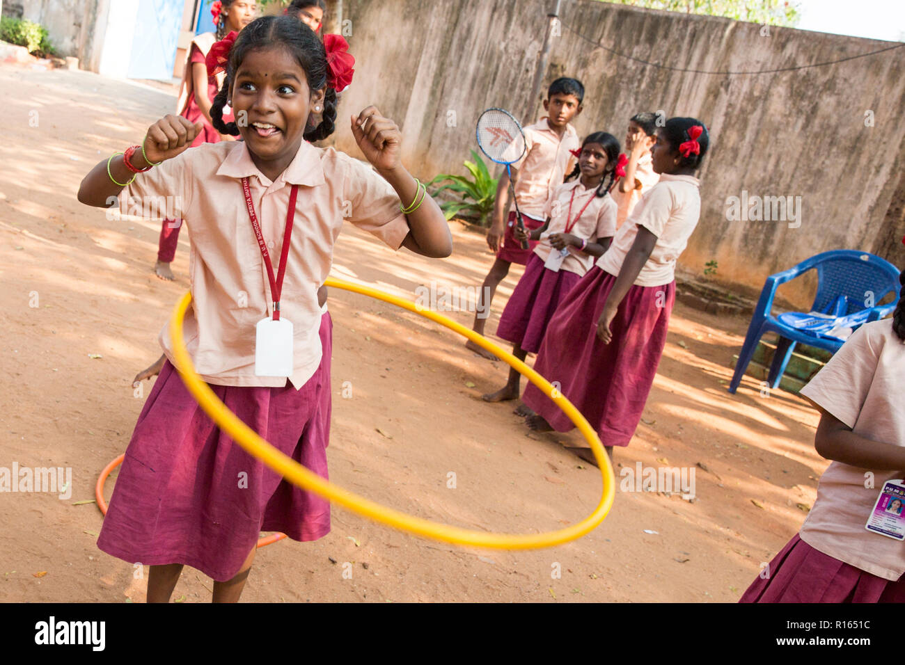 Niños jugando en un parque infantil con una niña haciendo hula hoop con una  chaqueta naranja fotos de archivo