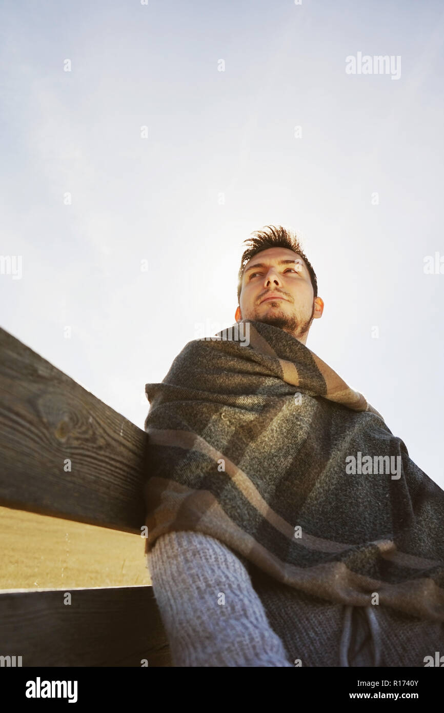 Una cabeza de hombre joven disfrutando de la tranquila mañana sol de otoño con la retroiluminación ilumina desde el cielo azul Foto de stock