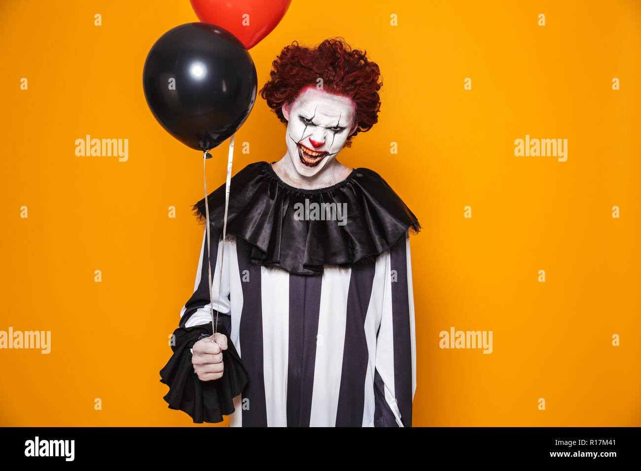 Payaso hombre vestido con traje negro y el maquillaje de halloween mirando  a la cámara aislada sobre fondo amarillo Fotografía de stock - Alamy