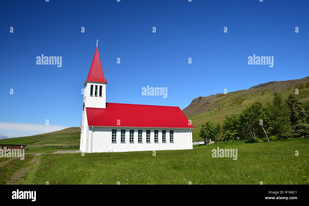 Una pequeña iglesia blanca en Islandia con un tejado rojo. El tiempo soleado y con un cielo azul. Foto de stock