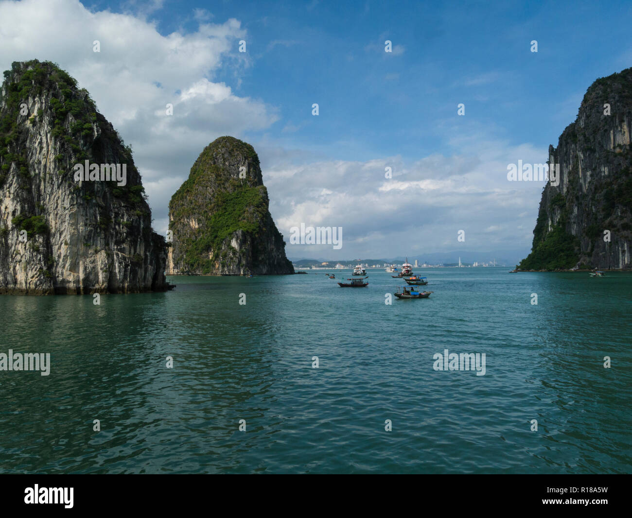 Los barcos de pesca y los barcos de crucero de basura turística en la Bahía de Halong en el Mar del Sur de China Vietnam Asia cruceros alrededor de la isla de piedra caliza espectaculares picos cubiertos en p Foto de stock