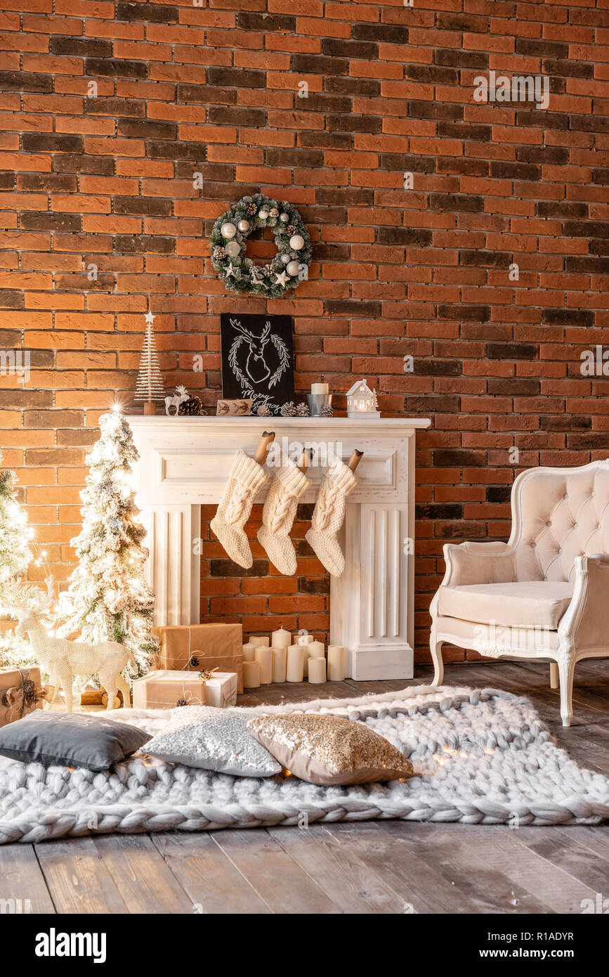 Apartamentos tipo loft, pared de ladrillo con velas y corona del árbol de  Navidad. Calcetines de lana blanca de Santa en la hoguera. Alfombra tejida  y silla, árbol de Navidad Fotografía de