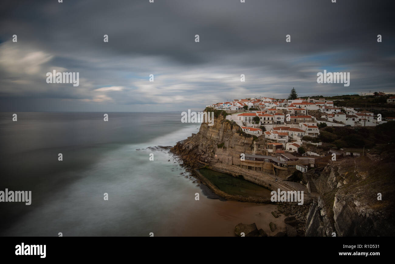Hermosas casas sobre un espolón rocoso situado en la localidad costera de Azenhas do Mar en el Océano Atlántico, Portugal con las olas chocando contra la costa. Foto de stock